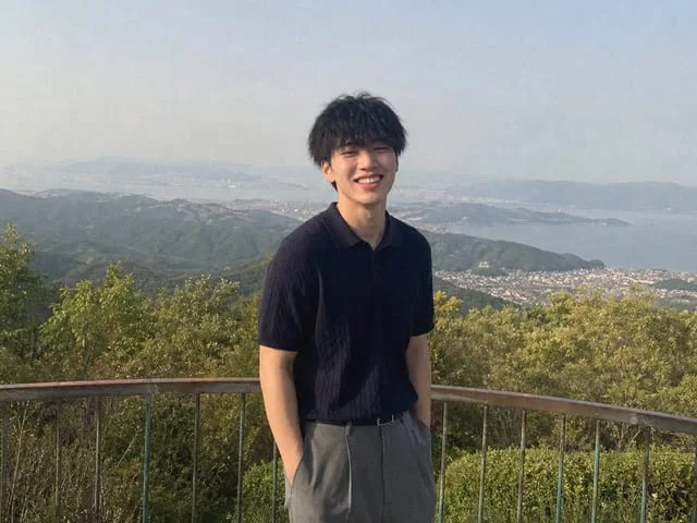 高台の展望デッキで、海と街を背に少し離れた位置から撮られた立ち姿